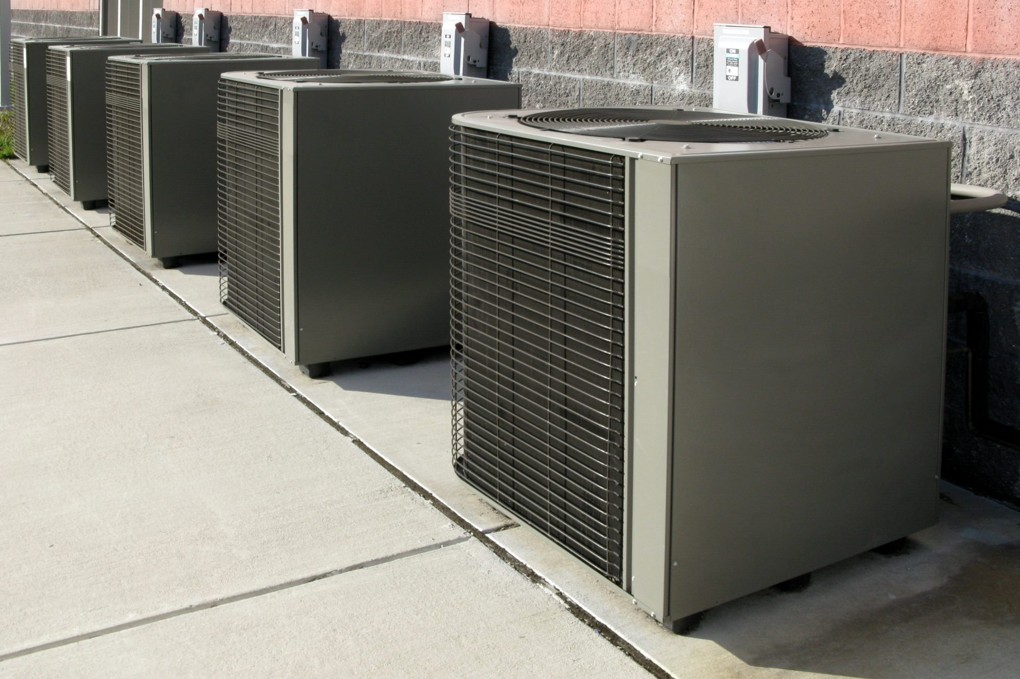 Air Conditioner Condenser AC Cooling System Units. Row of commercial HVAC air conditioner condenser units outside a commercial building as elements of a climate control cooling and refrigeration conditioning system